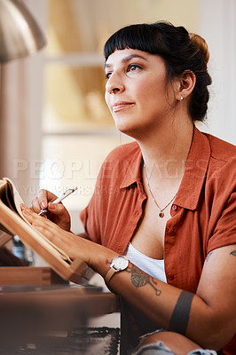 Buy stock photo Shot of a young woman looking thoughtful while sketching at home