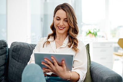 Buy stock photo Cropped shot of an attractive young businesswoman using a digital tablet while sitting on a sofa inside her office