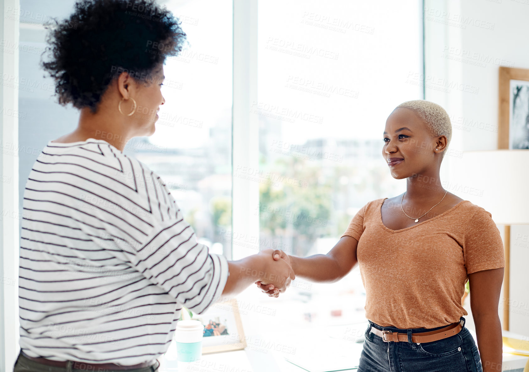 Buy stock photo Cropped shot of two attractive young businesswomen shaking hands together inside an office