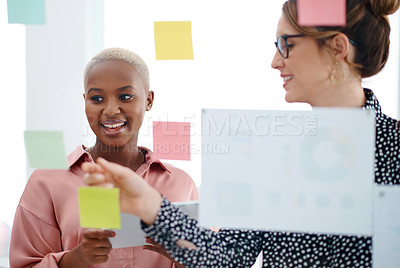 Buy stock photo Shot of two businesswomen brainstorming with notes on a glass wall in an office