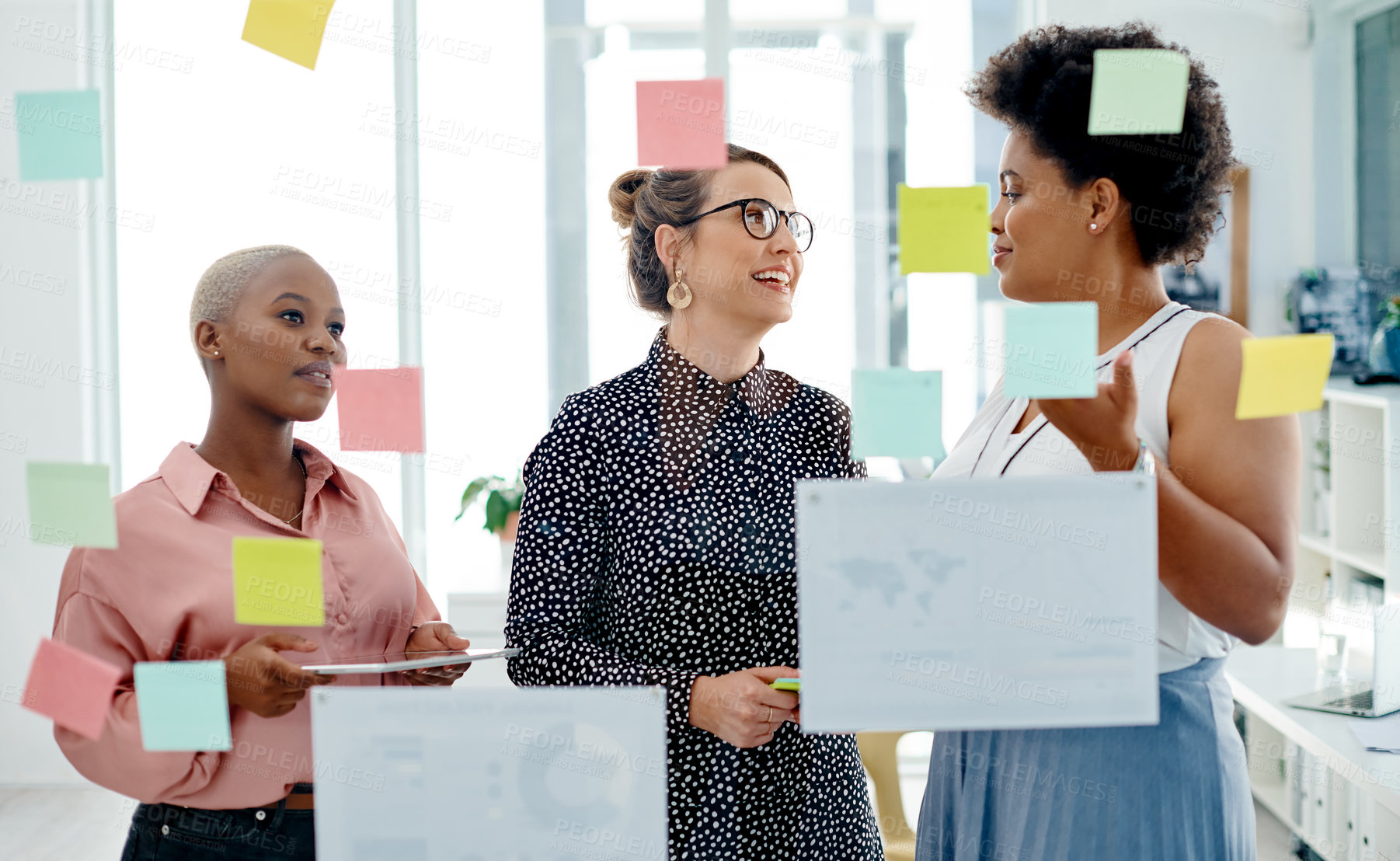 Buy stock photo Shot of a group of businesswomen brainstorming with notes on a glass wall in an office