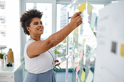 Buy stock photo Shot of a young businesswoman using a digital tablet while brainstorming with notes on a glass wall in an office