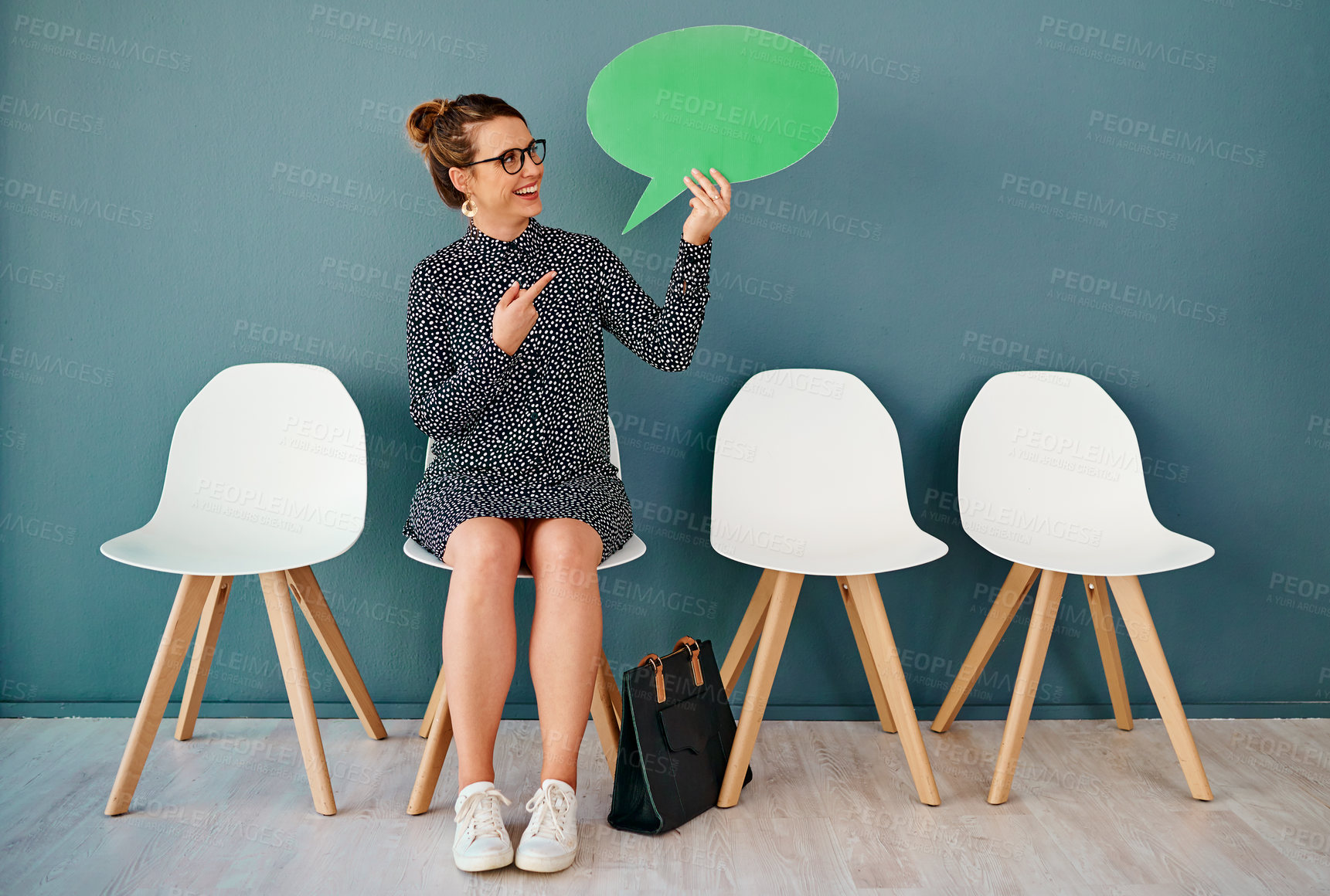 Buy stock photo Studio shot of an attractive young businesswoman pointing to a speech bubble while siting in line against a grey background