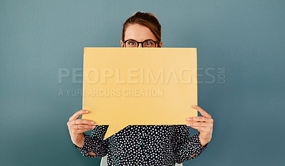 Buy stock photo Studio portrait of an attractive young businesswoman covering her face with a speech bubble while sitting against a grey background
