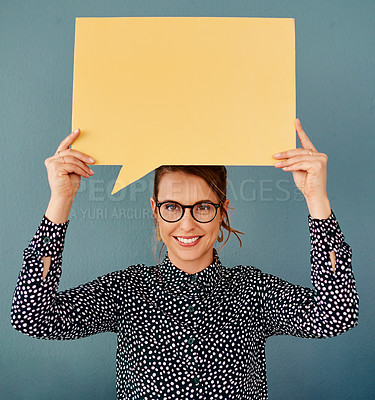 Buy stock photo Studio portrait of an attractive young businesswoman holding up a speech bubble while sitting against a grey background