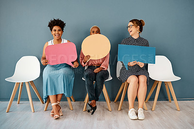 Buy stock photo Studio shot of a group of attractive young businesswomen holding speech bubbles while sitting in a row against a grey background