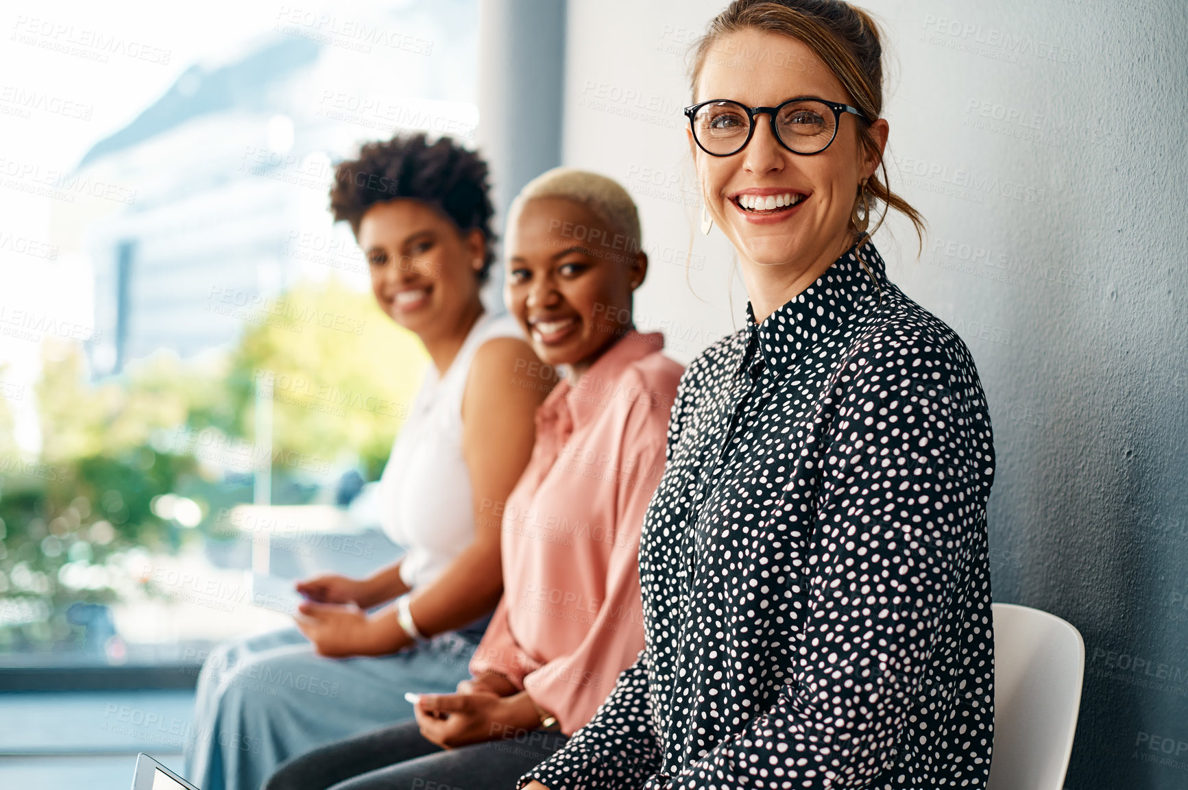 Buy stock photo Cropped portrait of a group of attractive young businesswomen smiling while sitting in line in a modern office