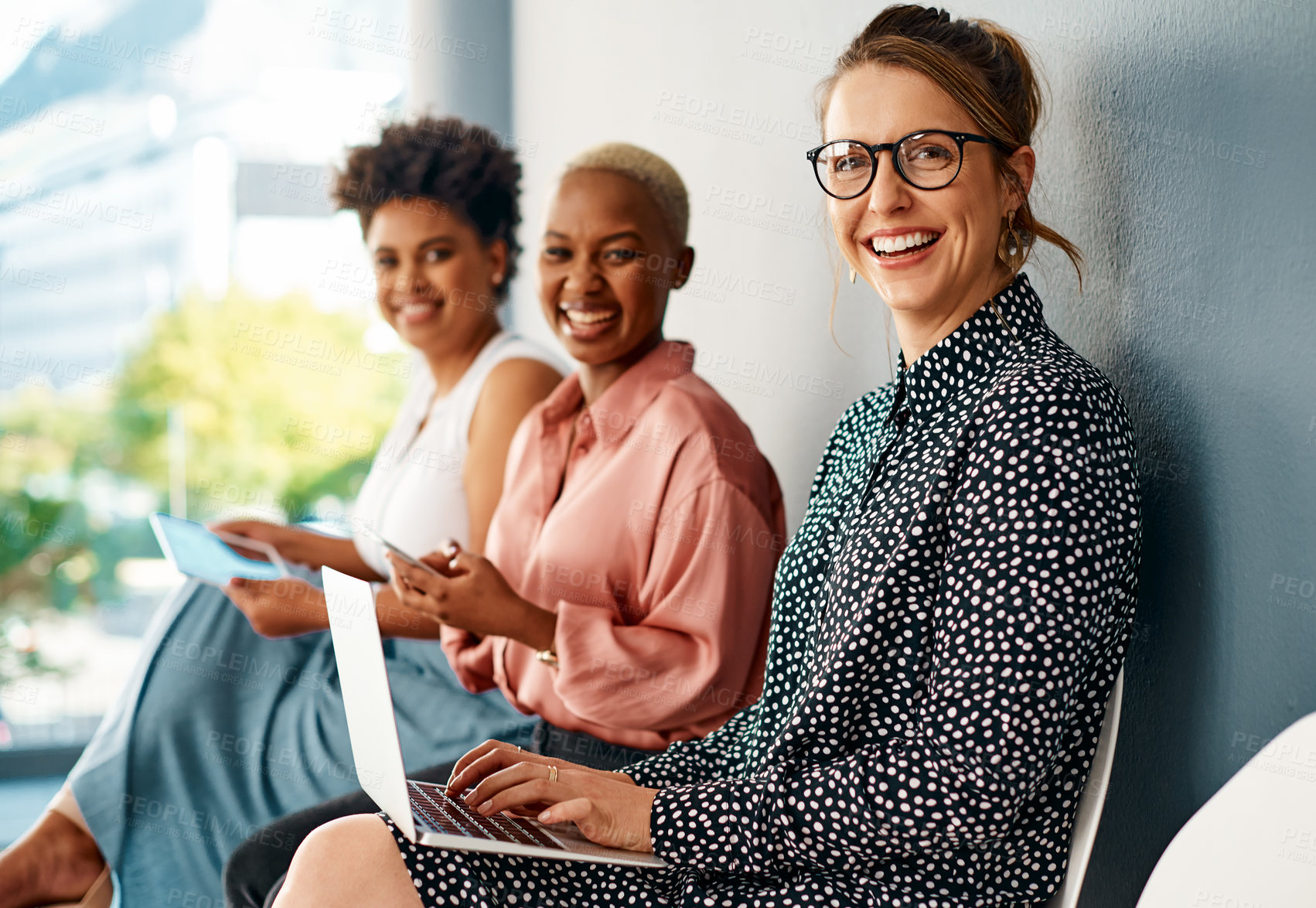 Buy stock photo Cropped portrait of a group of attractive young businesswomen using wireless technology while sitting in line in a modern office