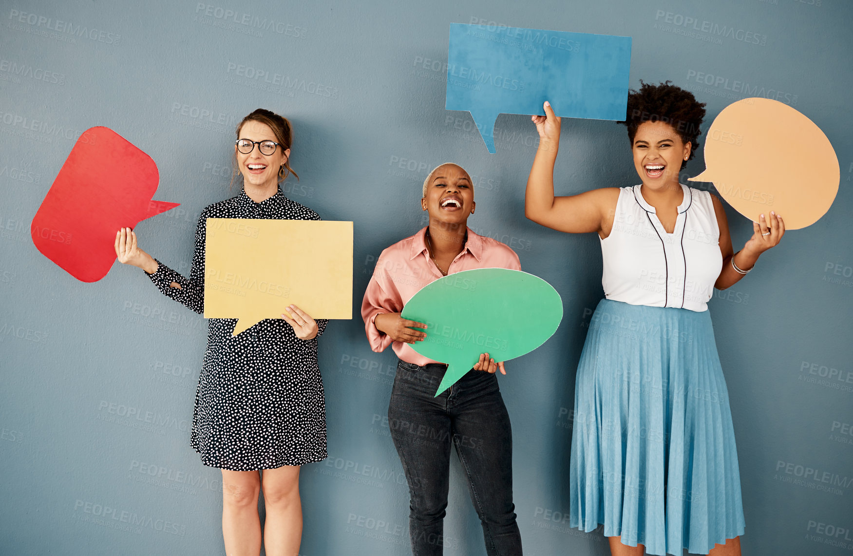 Buy stock photo Studio portrait of a group of attractive young businesswomen holding speech bubbles while standing against a grey background