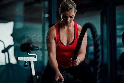 Buy stock photo Cropped shot of an attractive young female athlete working out with battle ropes in the gym