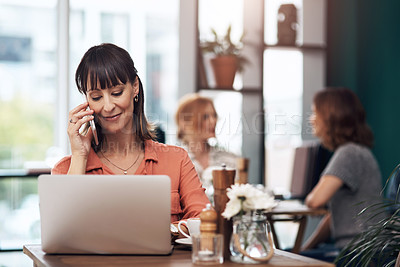 Buy stock photo Cropped shot of an attractive middle aged woman talking on her cellphone while working on a laptop inside of a coffee shop during the day
