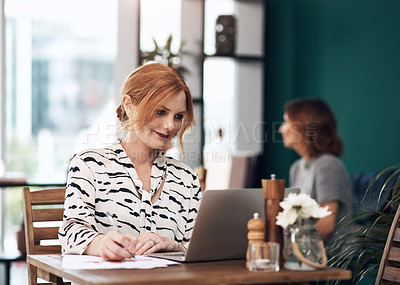 Buy stock photo Cropped shot of an attractive middle aged woman working on her laptop while making notes inside of a coffee shop during the day