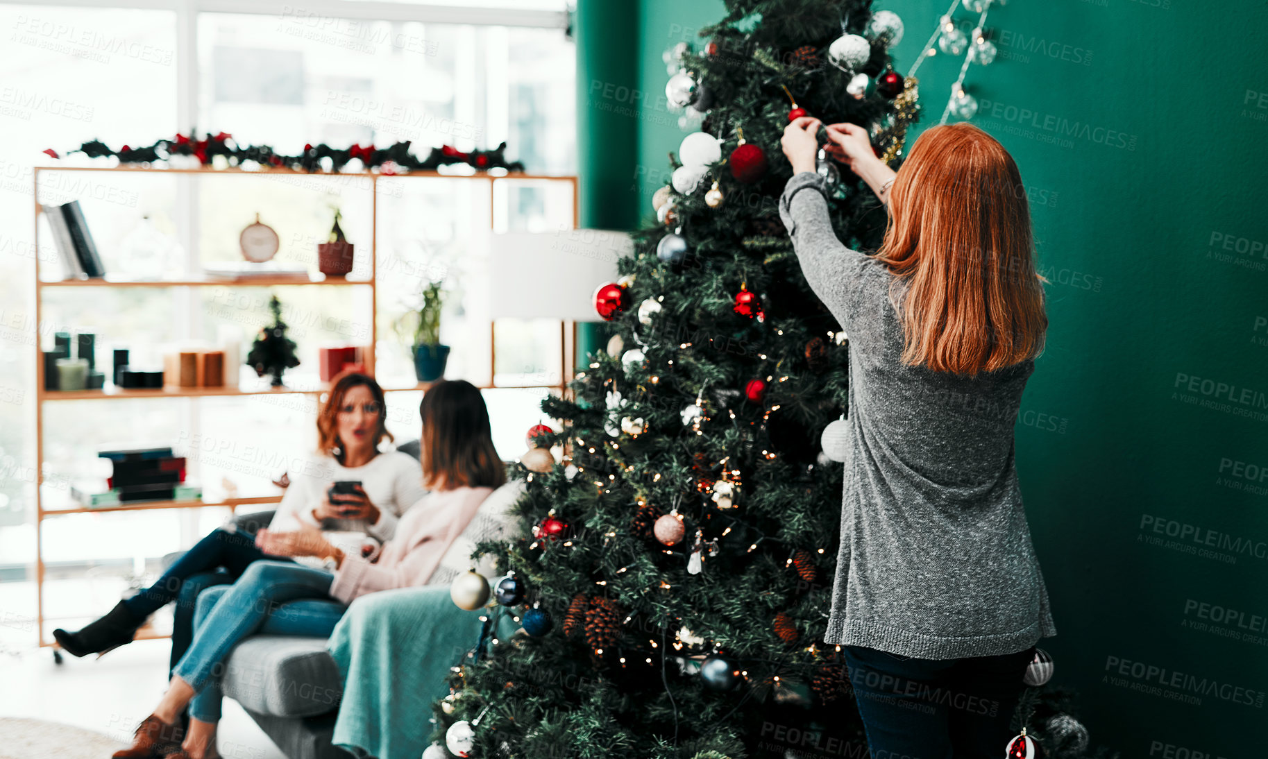 Buy stock photo Rearview shot of an unrecognisable woman decorating a Christmas tree at home during the day