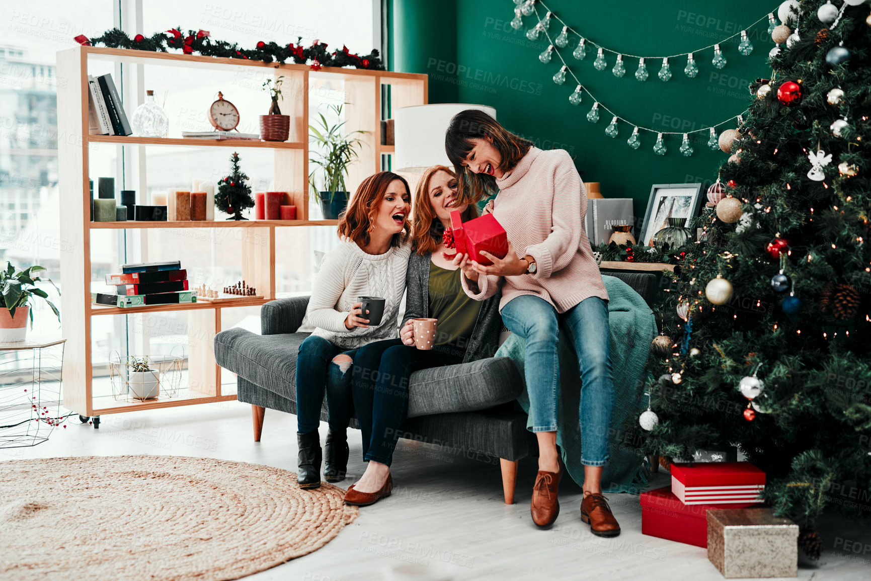 Buy stock photo Shot of three attractive middle aged women opening presents together while being seated on a sofa during Christmas time