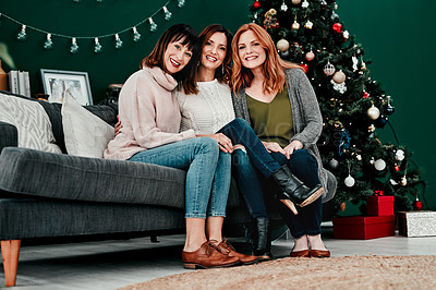 Buy stock photo Portrait of three attractive middle aged women seated together on a sofa with a Christmas tree in the background at home