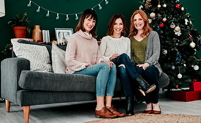 Buy stock photo Portrait of three attractive middle aged women seated together on a sofa with a Christmas tree in the background at home