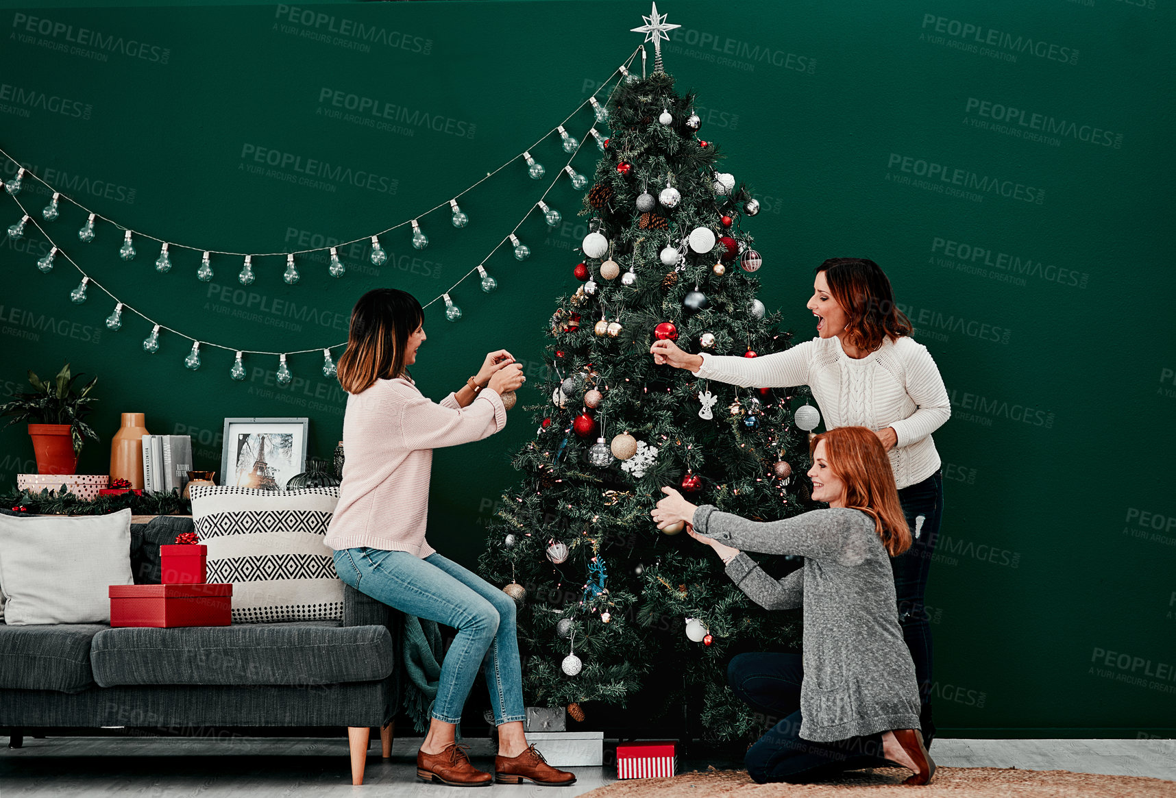 Buy stock photo Shot of three attractive middle aged women decorating a Christmas tree together at home