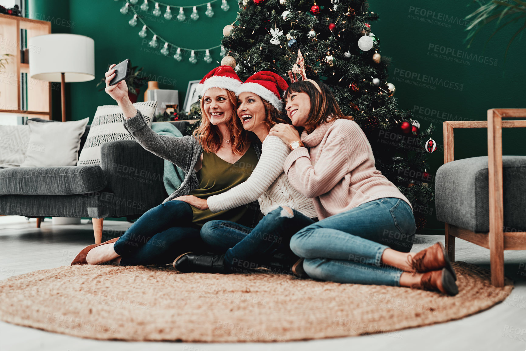 Buy stock photo Shot of three attractive middle aged women taking self portraits together with a cellphone at home during Christmas time