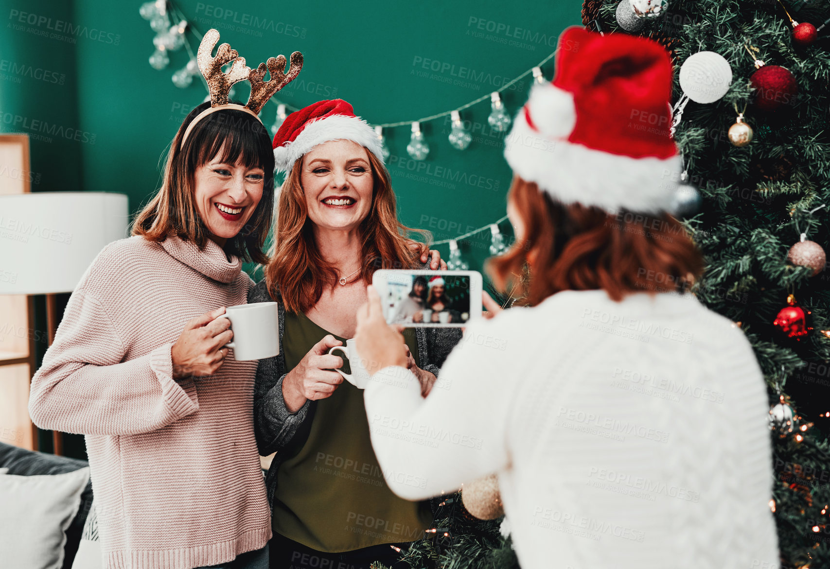 Buy stock photo Cropped shot of of a cheerful middle aged woman taking a picture of her two friends at home during Christmas time