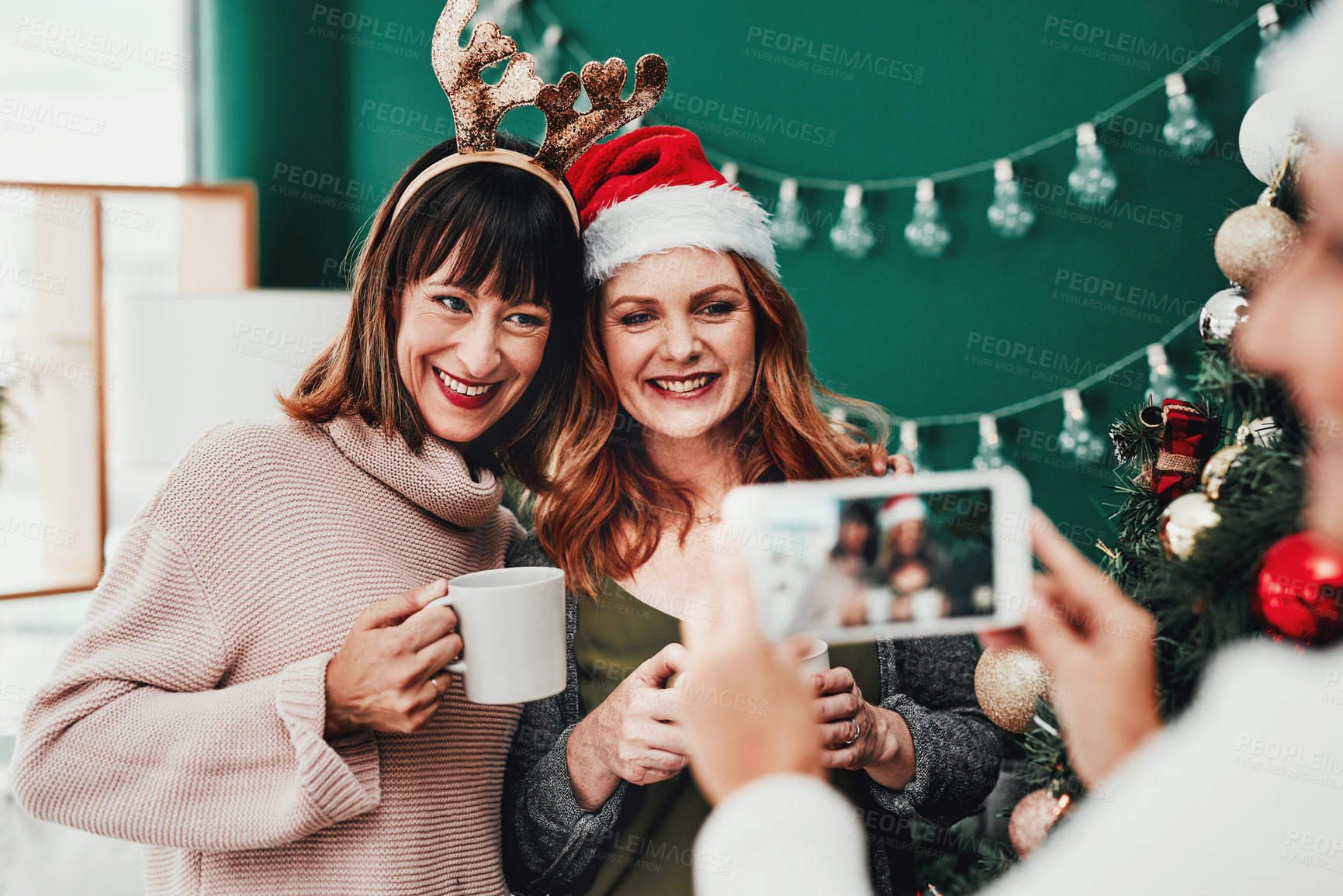 Buy stock photo Women, picture and happy for christmas with coffee mug, celebration and festive season at home. Friends, cozy for nostalgia and holiday tea time with smartphone photography, smile in lounge and love