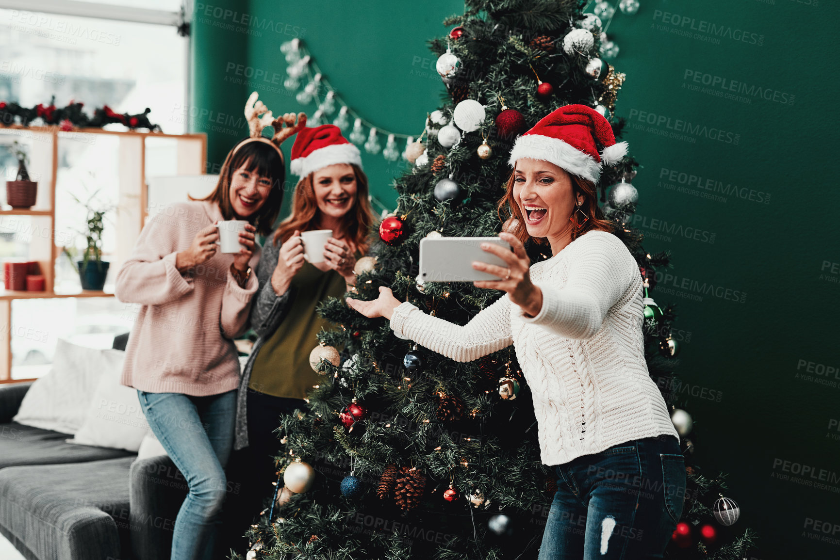 Buy stock photo Cropped shot of three attractive middle aged women taking self portraits together with a cellphone at home during Christmas time