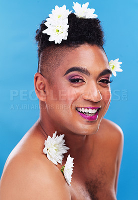 Buy stock photo Portrait of a gender fluid young man posing with flowers on his head against a blue background