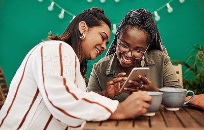 Buy stock photo Shot of two young women using a smartphone together at a cafe