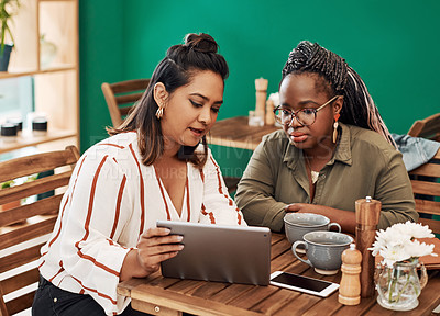 Buy stock photo Shot of two young women using a digital tablet together at a cafe