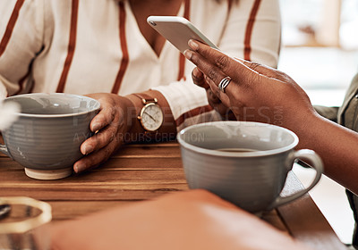 Buy stock photo Cropped shot of two women using a smartphone together at a cafe