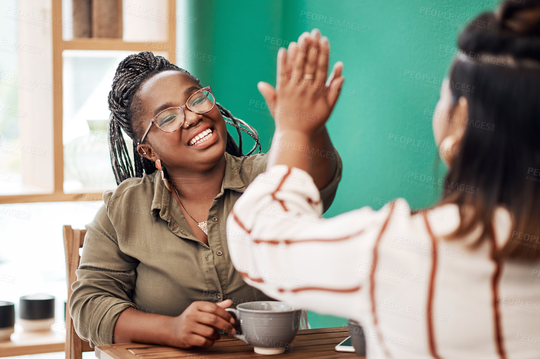 Buy stock photo Shot of two young women giving each other a high five in a cafe