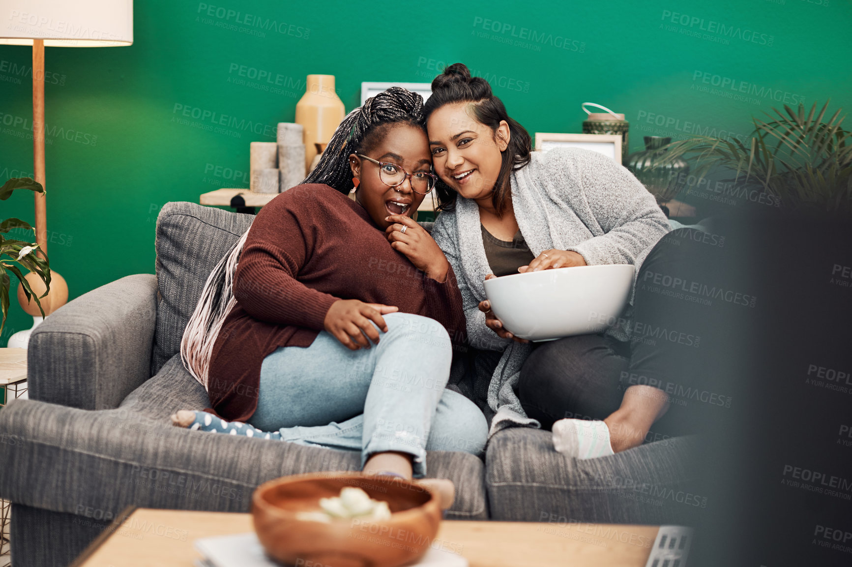 Buy stock photo Girl friends, shocking movie and home living room laughing on a couch with a happy smile. Tv, relax and women together in a lounge with a female friend looking at a television in house with popcorn