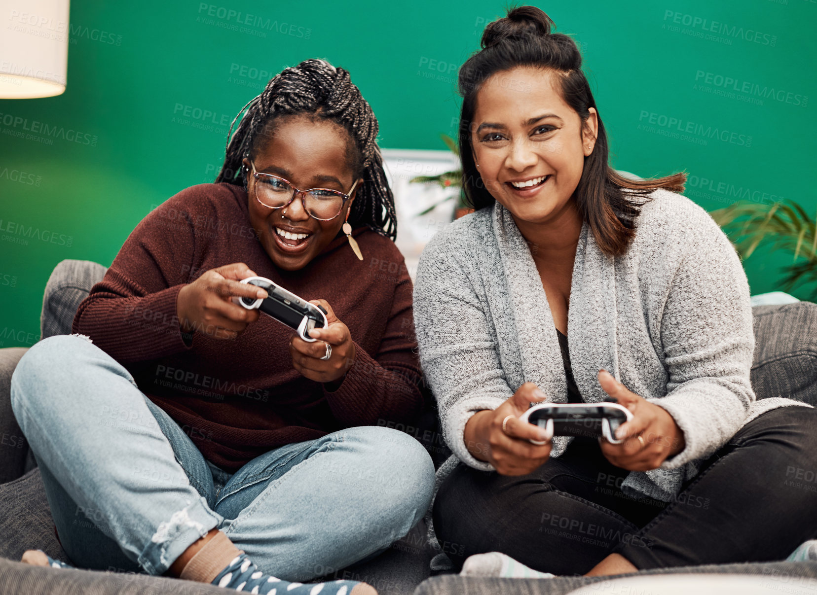 Buy stock photo Shot of two young women playing video games on the sofa at home