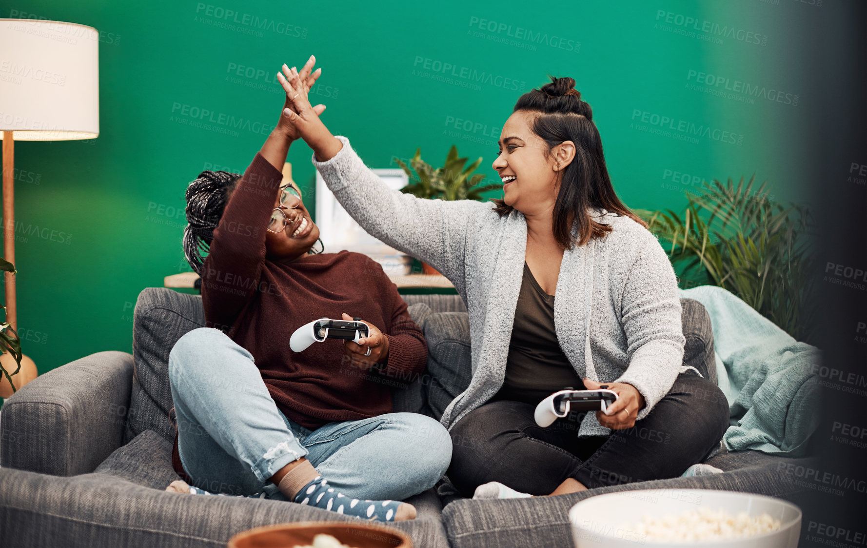 Buy stock photo Shot of two young women giving each other a high five while playing video games on the sofa at home