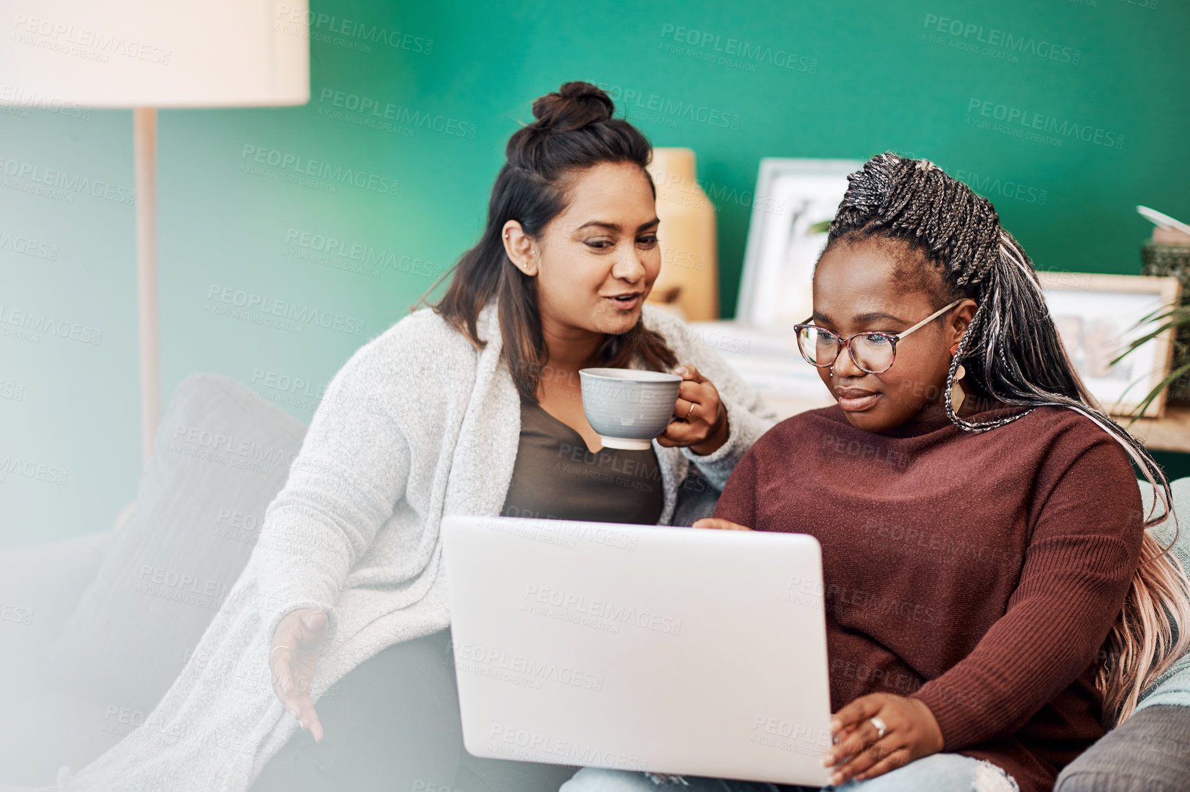Buy stock photo Shot of two young women using a laptop on the sofa at home