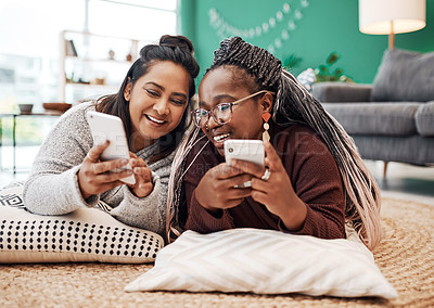 Buy stock photo Shot of two young women using their smartphones on the floor at home