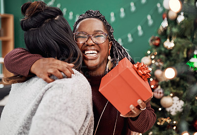 Buy stock photo Shot of two happy young women exchanging gifts during Christmas at home