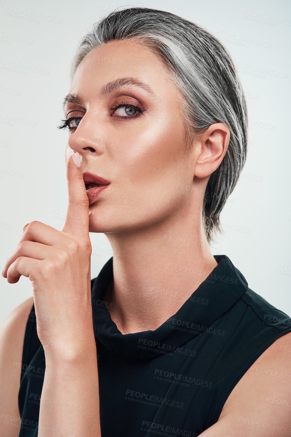 Buy stock photo Studio portrait of a beautiful mature woman posing with her finger on her lips against a grey background