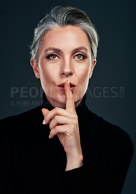 Buy stock photo Studio portrait of a beautiful mature woman posing with her finger on her lips against a dark background