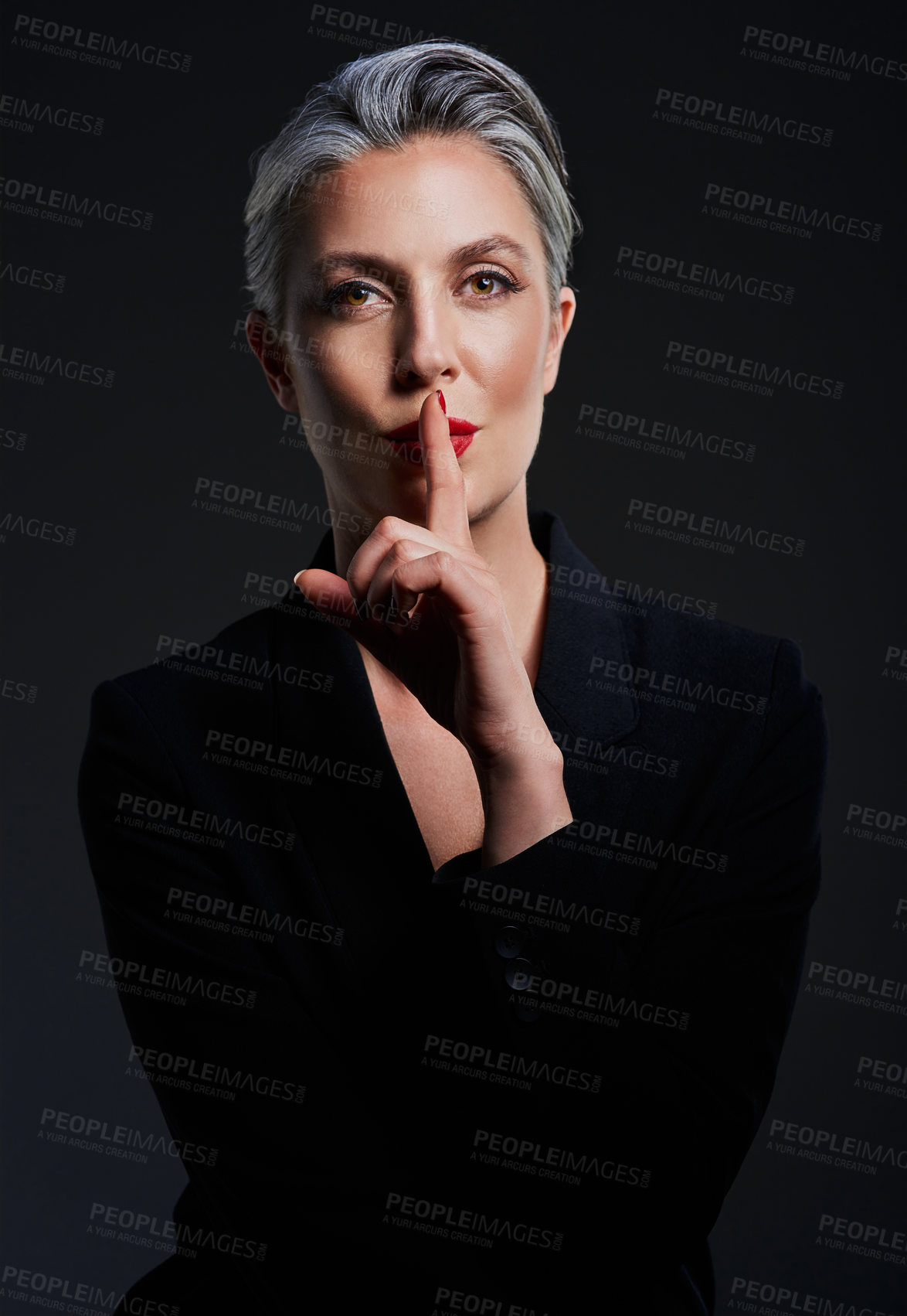 Buy stock photo Studio portrait of a beautiful mature woman posing with her finger on her lips against a dark background