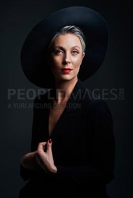 Buy stock photo Studio portrait of a beautiful mature woman wearing a hat and posing against a dark background