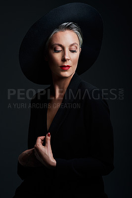 Buy stock photo Studio shot of a beautiful mature woman wearing a hat and posing against a dark background