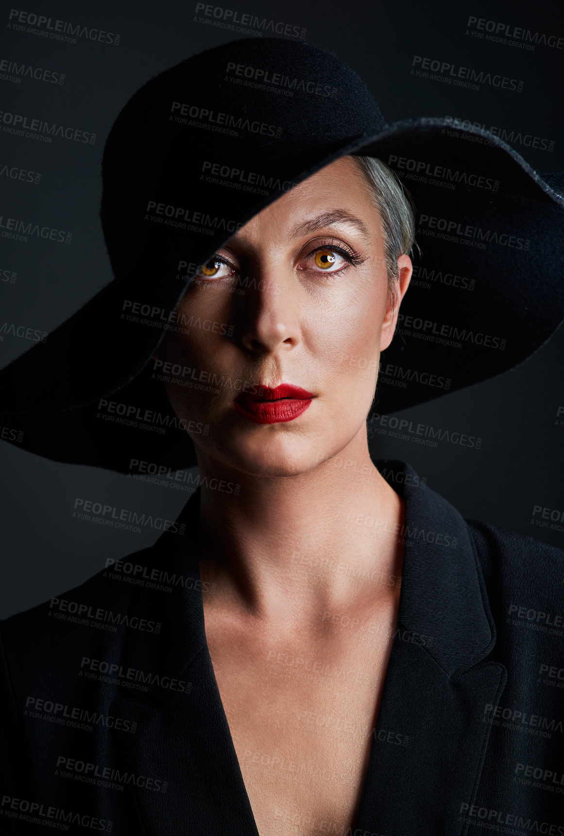 Buy stock photo Studio portrait of a beautiful mature woman wearing a hat and posing against a dark background