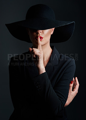 Buy stock photo Studio shot of a beautiful mature woman wearing a hat and posing with her finger on her lips against a dark background