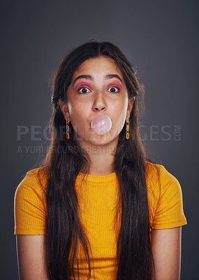 Buy stock photo Cropped portrait of an attractive teenage girl standing against a dark background alone and blowing bubbles with bubblegum