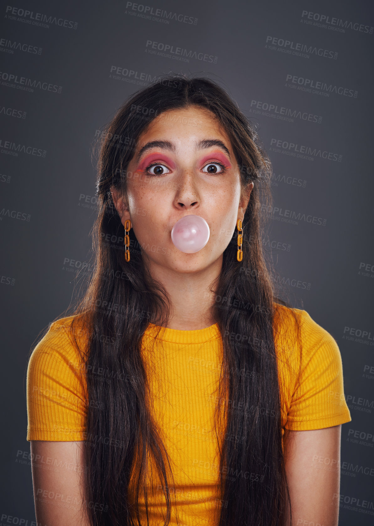 Buy stock photo Cropped portrait of an attractive teenage girl standing against a dark background alone and blowing bubbles with bubblegum