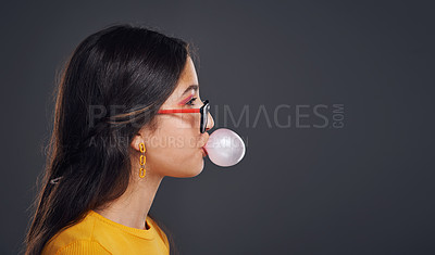 Buy stock photo Cropped shot of an attractive teenage girl standing against a dark background alone and blowing bubbles with bubblegum