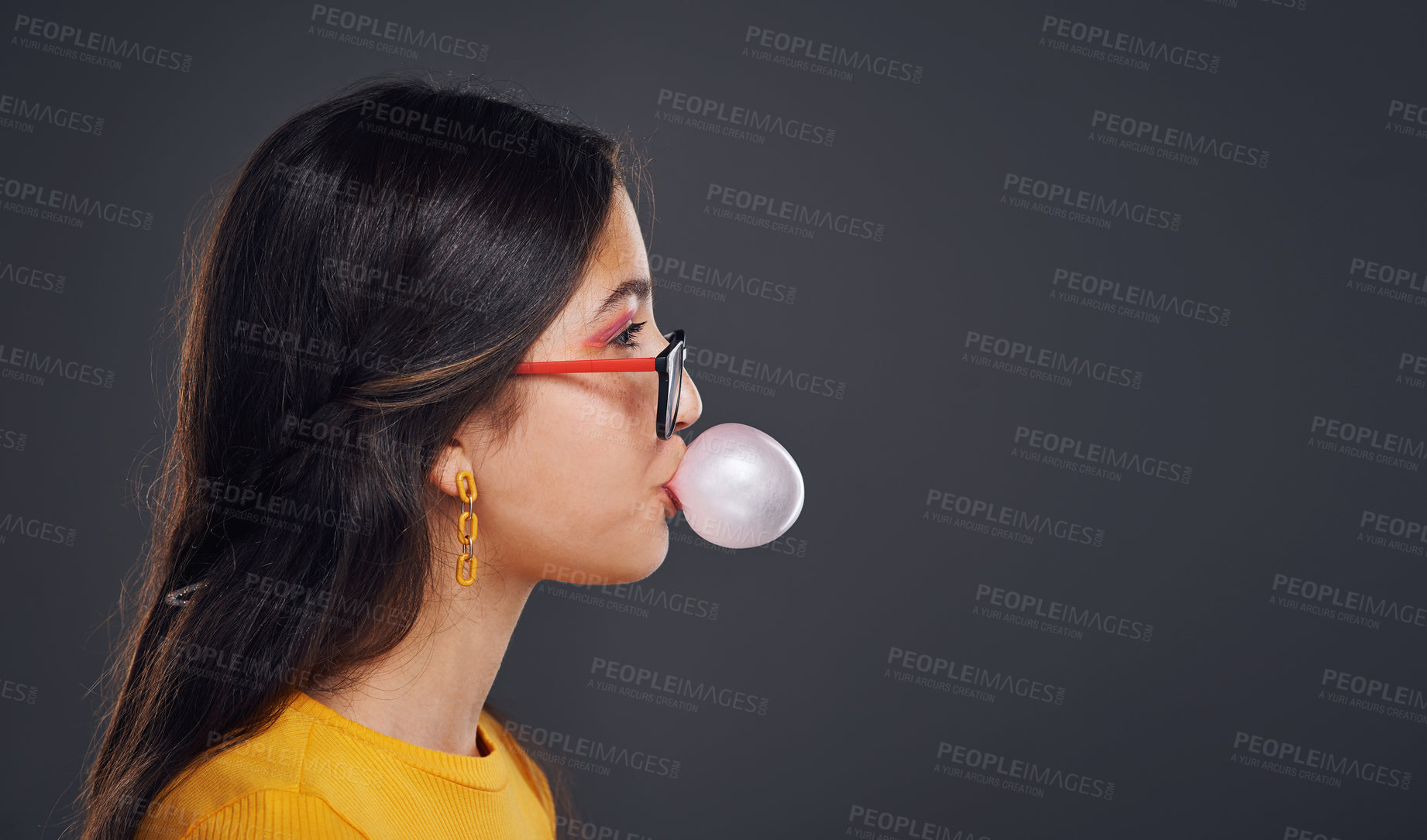 Buy stock photo Cropped shot of an attractive teenage girl standing against a dark background alone and blowing bubbles with bubblegum