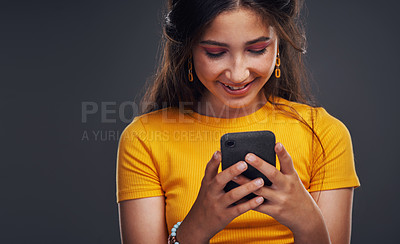 Buy stock photo Cropped shot of an attractive teenage girl standing against a dark background and using her cellphone in the studio