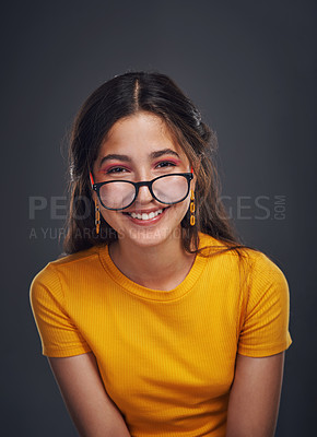 Buy stock photo Cropped portrait of an attractive teenage girl wearing glasses and standing against a dark background in the studio alone