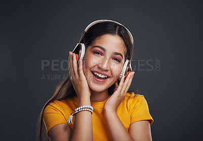 Buy stock photo Cropped portrait of an attractive teenage girl standing against a dark background alone and listening to music through headphones
